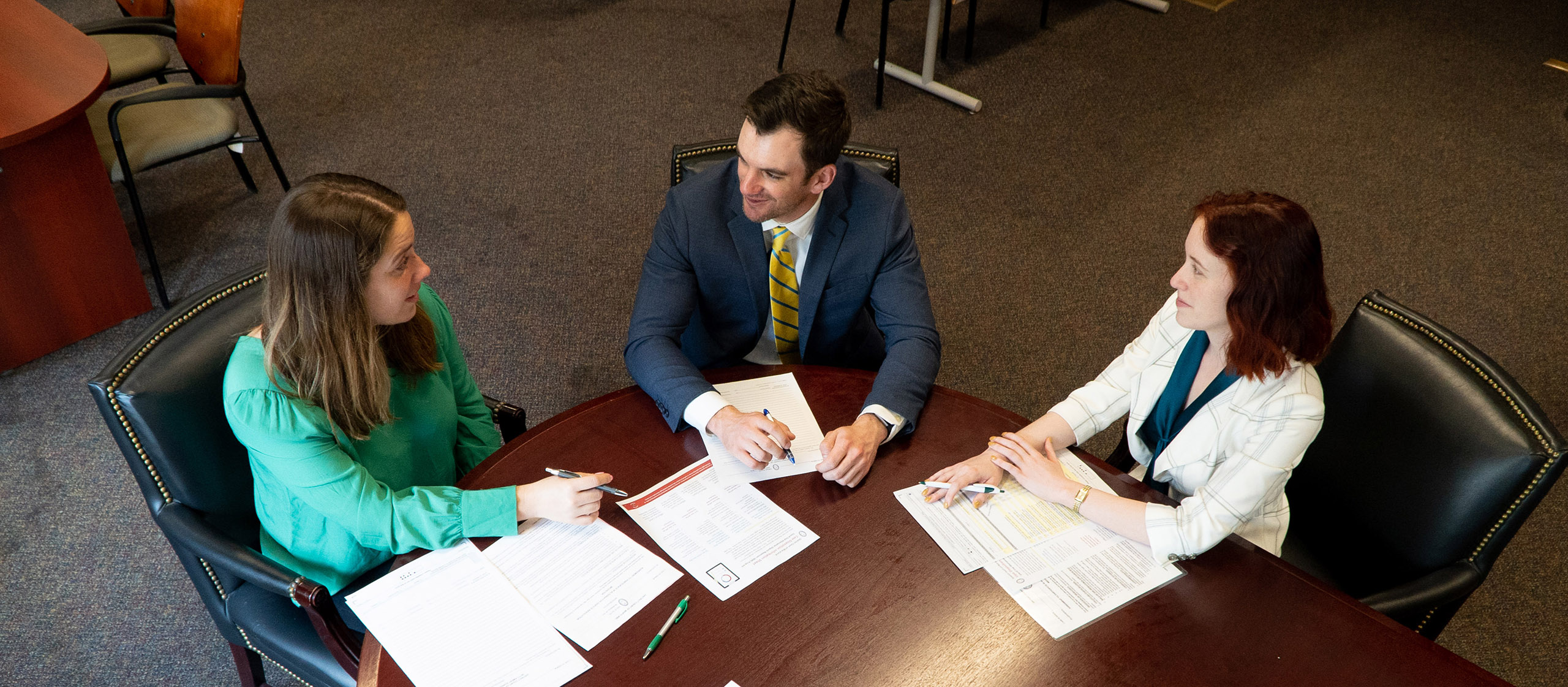 three professionals at a round table talking, papers spread around