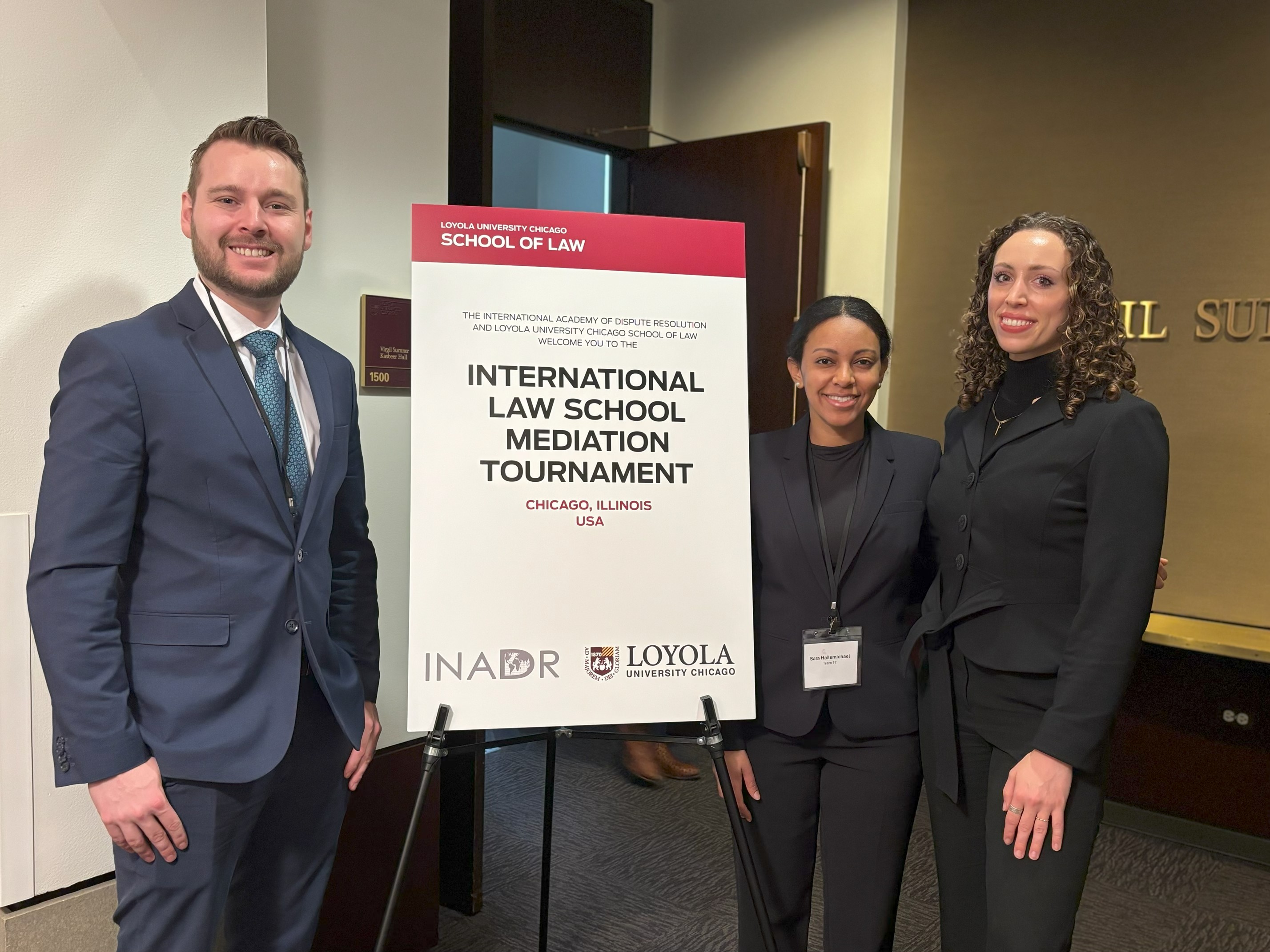 People standing in front of a sign for the International Law School Mediation Tournament
