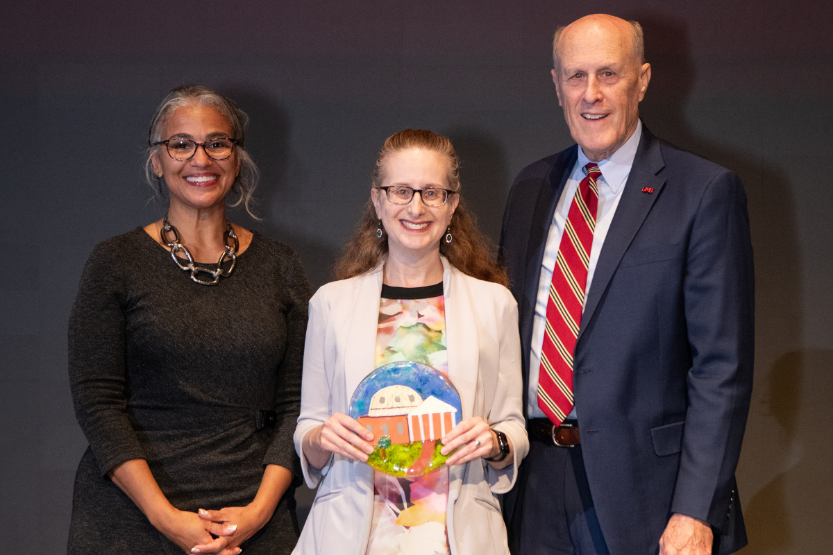 Three people posing in business attire with an award